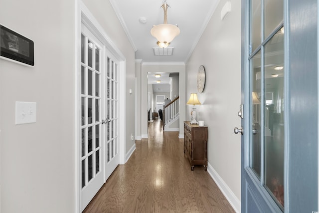 hall with wood finished floors, crown molding, baseboards, stairway, and french doors