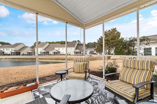 sunroom / solarium featuring a wealth of natural light, vaulted ceiling, a residential view, and a water view