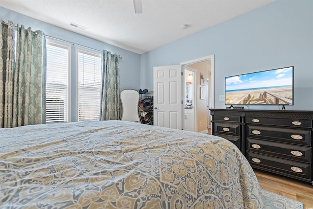 bedroom with a ceiling fan, wood finished floors, visible vents, and a textured ceiling