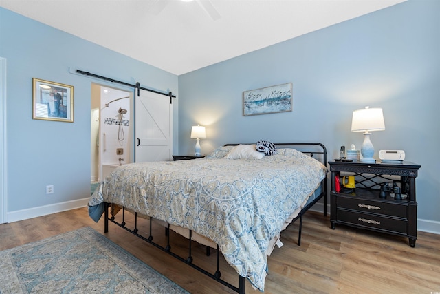 bedroom featuring ceiling fan, baseboards, a barn door, and wood finished floors