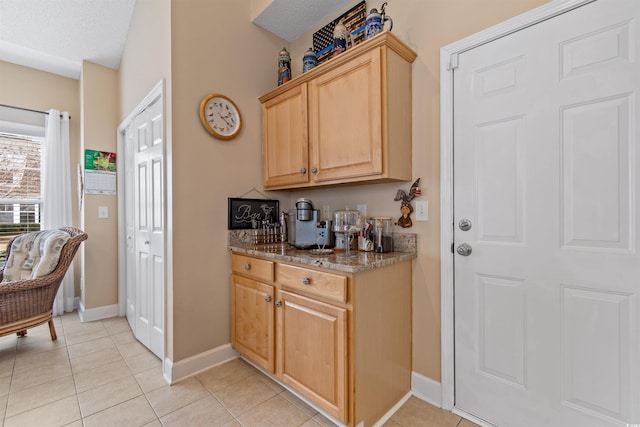 kitchen featuring light brown cabinets, stone countertops, a textured ceiling, light tile patterned floors, and baseboards