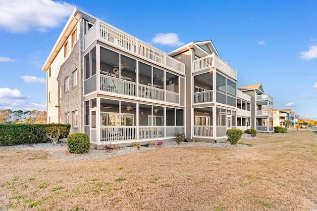 back of property featuring a balcony, a lawn, a ceiling fan, and a sunroom