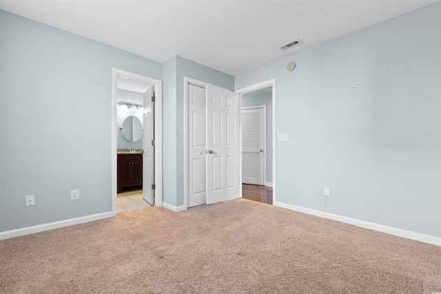 unfurnished bedroom with visible vents, baseboards, light colored carpet, a closet, and ensuite bath