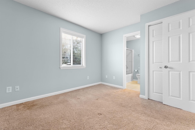 unfurnished bedroom with connected bathroom, a textured ceiling, baseboards, and carpet floors