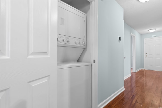 laundry room with baseboards, laundry area, stacked washing maching and dryer, wood finished floors, and a textured ceiling