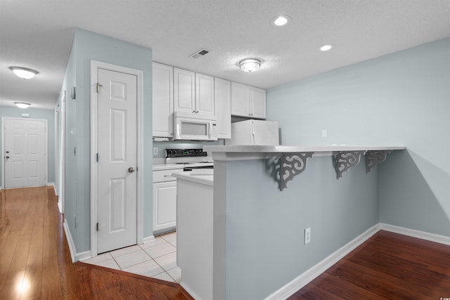 kitchen featuring visible vents, white appliances, a breakfast bar area, white cabinets, and light wood finished floors