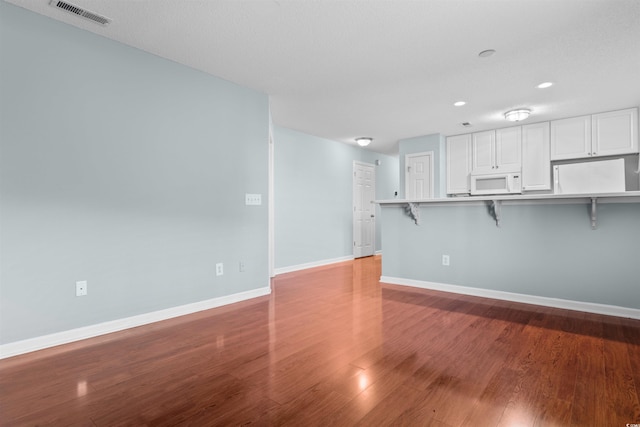 kitchen featuring a breakfast bar area, wood finished floors, white microwave, visible vents, and baseboards