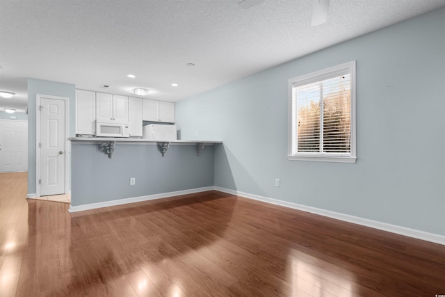 kitchen with white cabinetry, white appliances, wood finished floors, and baseboards