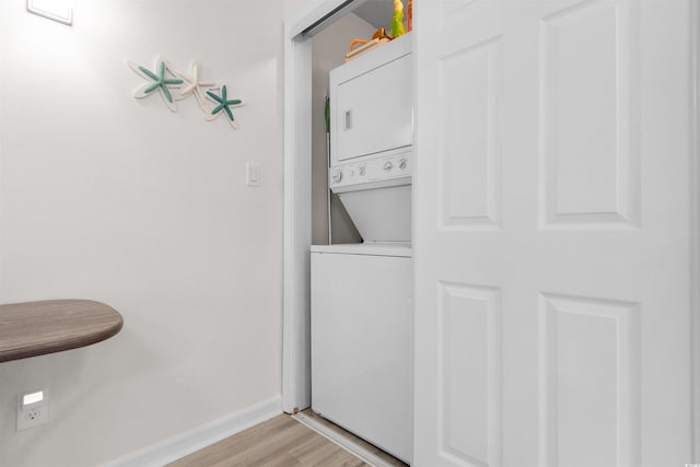 laundry room with laundry area, stacked washer and clothes dryer, light wood-style flooring, and baseboards