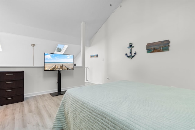 bedroom featuring baseboards, lofted ceiling with skylight, and light wood-style floors