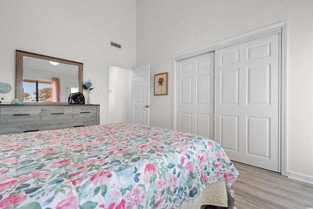 bedroom featuring a high ceiling, visible vents, light wood finished floors, and a closet