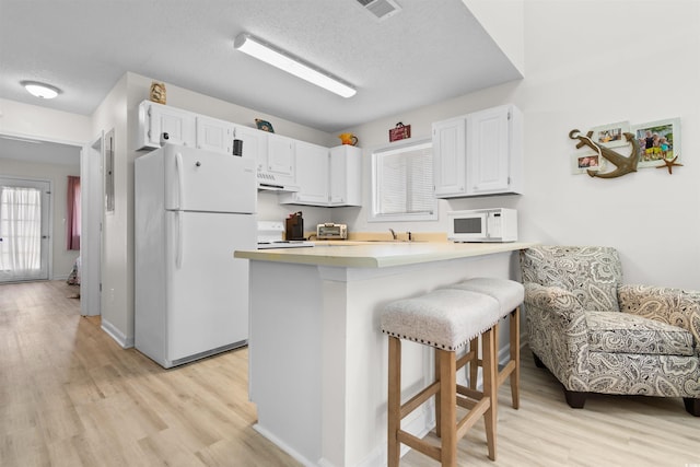 kitchen with light wood-style flooring, under cabinet range hood, white cabinets, and white appliances
