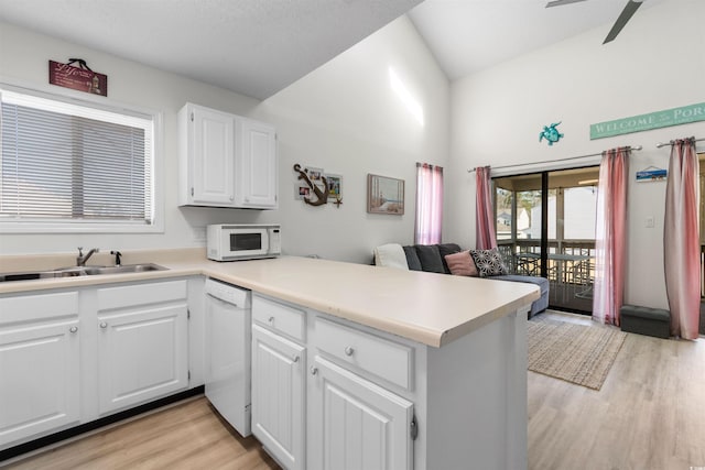 kitchen featuring a sink, a peninsula, light wood-style floors, white appliances, and white cabinetry