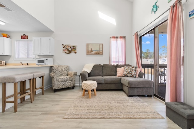 living room with visible vents, light wood finished floors, a towering ceiling, and baseboards