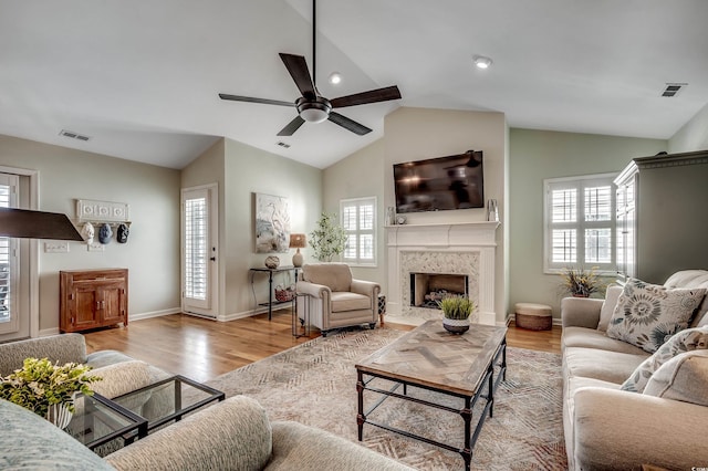 living area featuring a high end fireplace, light wood-style flooring, ceiling fan, and vaulted ceiling