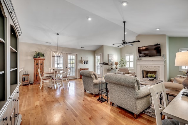 living room with light wood finished floors, ceiling fan with notable chandelier, a fireplace, and lofted ceiling