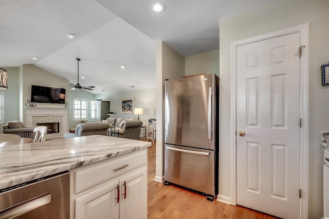 kitchen with light wood finished floors, a fireplace, freestanding refrigerator, ceiling fan, and vaulted ceiling