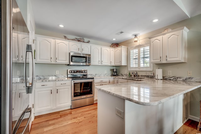 kitchen with visible vents, a peninsula, white cabinets, stainless steel appliances, and a sink