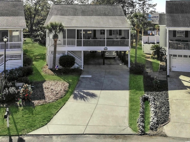 coastal inspired home featuring a shingled roof, stairway, concrete driveway, a sunroom, and a carport