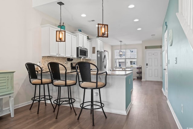 kitchen featuring backsplash, appliances with stainless steel finishes, a peninsula, white cabinets, and dark wood-style flooring