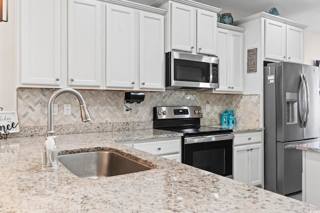 kitchen with light stone countertops, a sink, decorative backsplash, stainless steel appliances, and white cabinetry