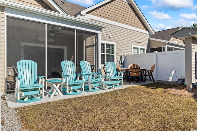 rear view of house featuring a shingled roof, fence, a lawn, a sunroom, and a patio area