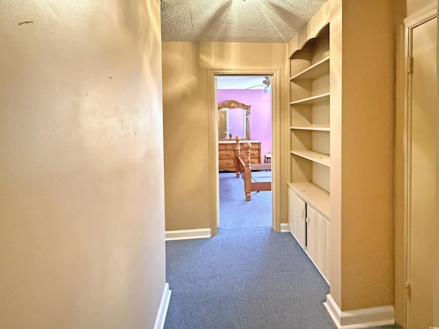 corridor with baseboards, a textured ceiling, and dark carpet