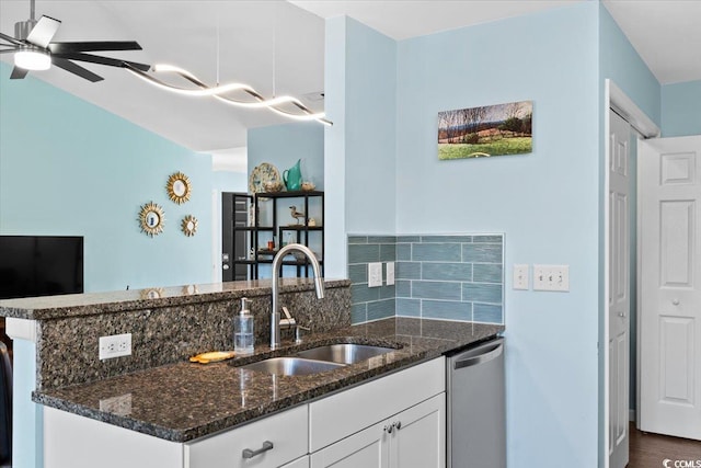 kitchen featuring a sink, stainless steel dishwasher, white cabinetry, dark stone counters, and a peninsula