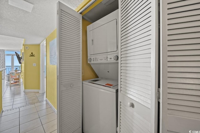 laundry room featuring a textured ceiling, stacked washing maching and dryer, light tile patterned flooring, baseboards, and laundry area