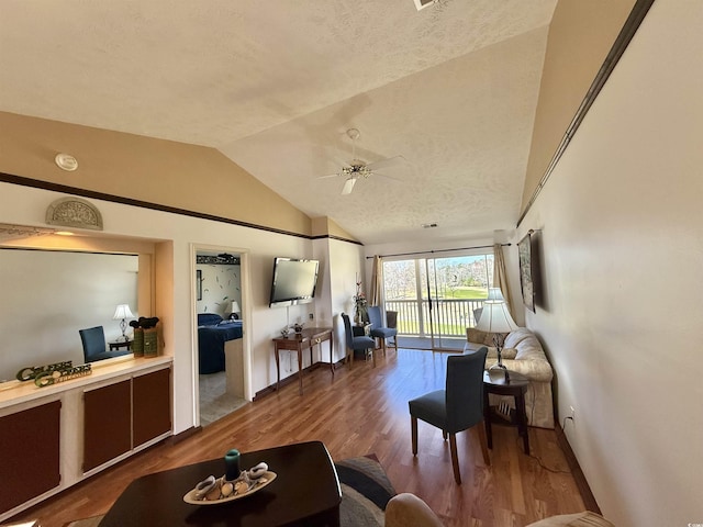 living room with a ceiling fan, a textured ceiling, wood finished floors, baseboards, and vaulted ceiling