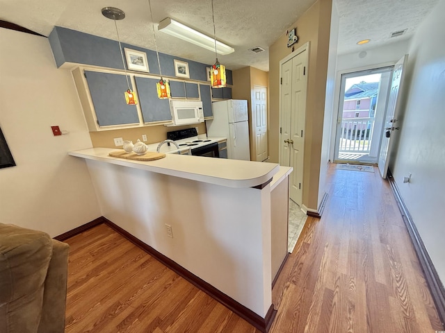 kitchen featuring a textured ceiling, wood finished floors, white appliances, a peninsula, and light countertops