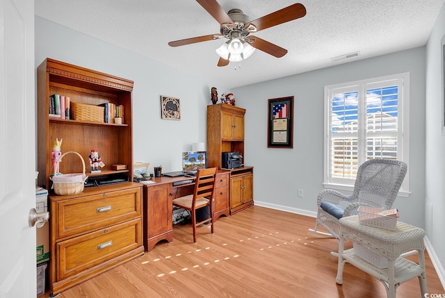 office featuring a ceiling fan, baseboards, visible vents, light wood finished floors, and a textured ceiling