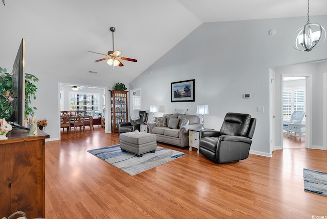 living area with visible vents, high vaulted ceiling, light wood-style flooring, ceiling fan with notable chandelier, and baseboards