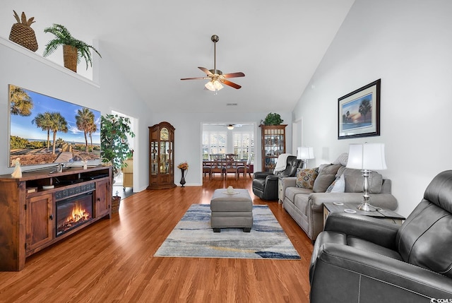 living room featuring a glass covered fireplace, wood finished floors, high vaulted ceiling, and ceiling fan