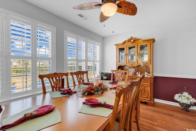 dining room featuring light wood finished floors, visible vents, baseboards, ceiling fan, and a textured ceiling