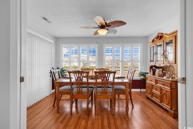 dining space featuring visible vents, wood finished floors, a textured ceiling, and ceiling fan