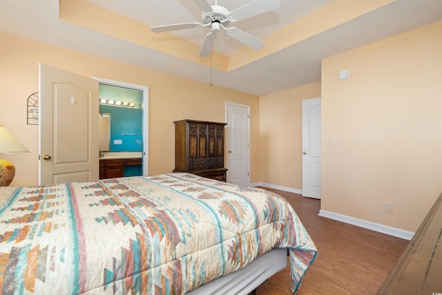 bedroom with a raised ceiling, wood finished floors, connected bathroom, baseboards, and ceiling fan