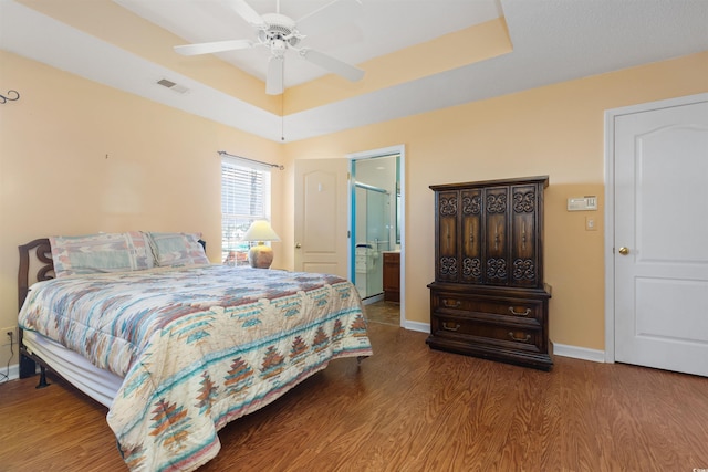 bedroom featuring a raised ceiling, wood finished floors, visible vents, and baseboards