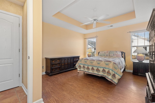 bedroom with a tray ceiling, multiple windows, wood finished floors, and baseboards