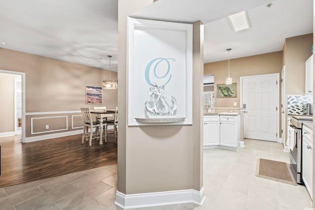 kitchen featuring hanging light fixtures, light countertops, stainless steel range with electric stovetop, white cabinets, and tasteful backsplash