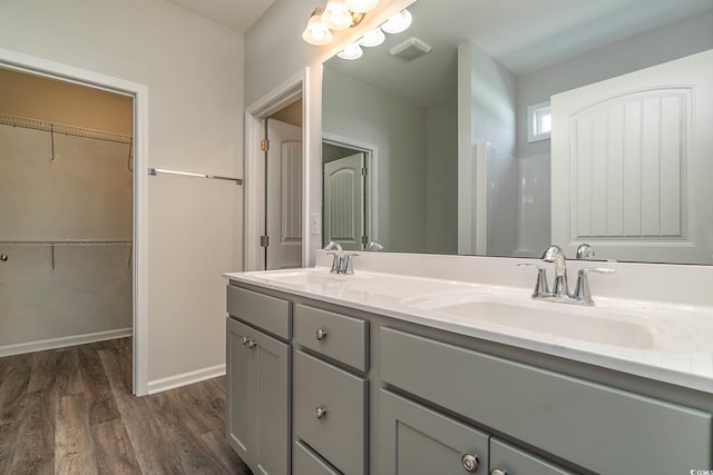 bathroom featuring double vanity, wood finished floors, a walk in closet, and a sink