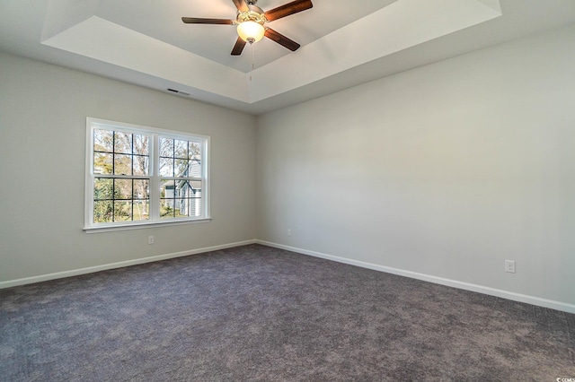 spare room with a tray ceiling, a ceiling fan, baseboards, and dark carpet