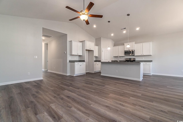 kitchen with dark wood-type flooring, a ceiling fan, dark countertops, open floor plan, and appliances with stainless steel finishes