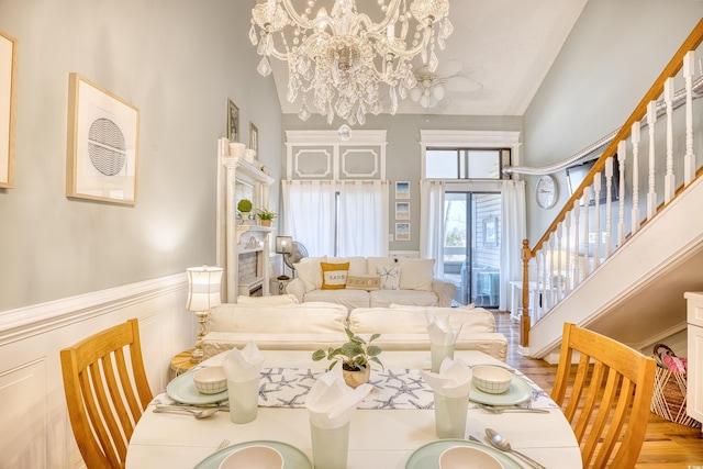 dining area featuring a wainscoted wall, wood finished floors, stairway, a decorative wall, and a chandelier