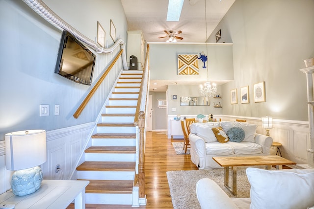 living room with stairway, wood finished floors, a skylight, a towering ceiling, and wainscoting