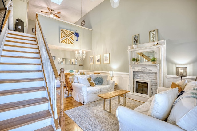 living area with stairway, wainscoting, ceiling fan with notable chandelier, wood finished floors, and high vaulted ceiling