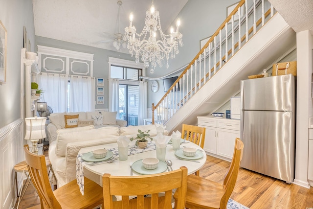 dining space with light wood-style flooring, stairway, an inviting chandelier, wainscoting, and a decorative wall