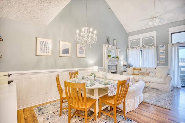 dining area featuring a wainscoted wall, high vaulted ceiling, ceiling fan with notable chandelier, a textured ceiling, and wood finished floors