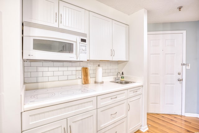 kitchen with a sink, backsplash, white appliances, light wood-style floors, and light countertops