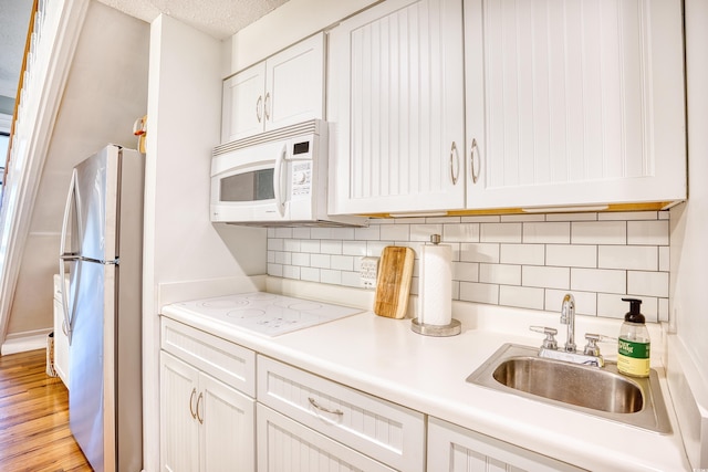 kitchen with a sink, white cabinetry, white appliances, light countertops, and decorative backsplash